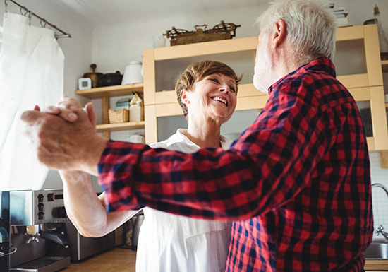 elderly couple smiling and dancing in their kitchen