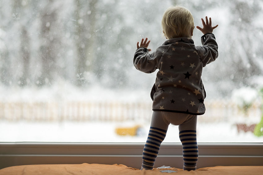 child looking out window at snow