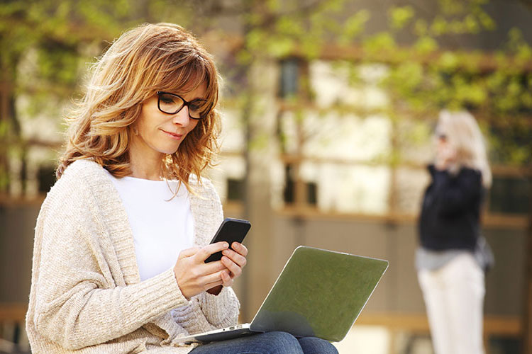 woman sitting with laptop looking at phone