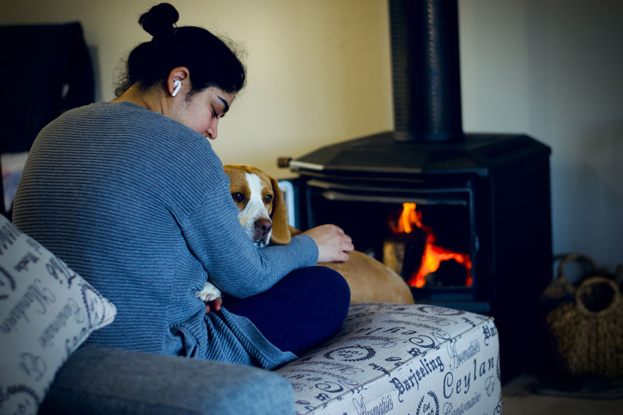 A woman and a dog relax in front of a fire place.