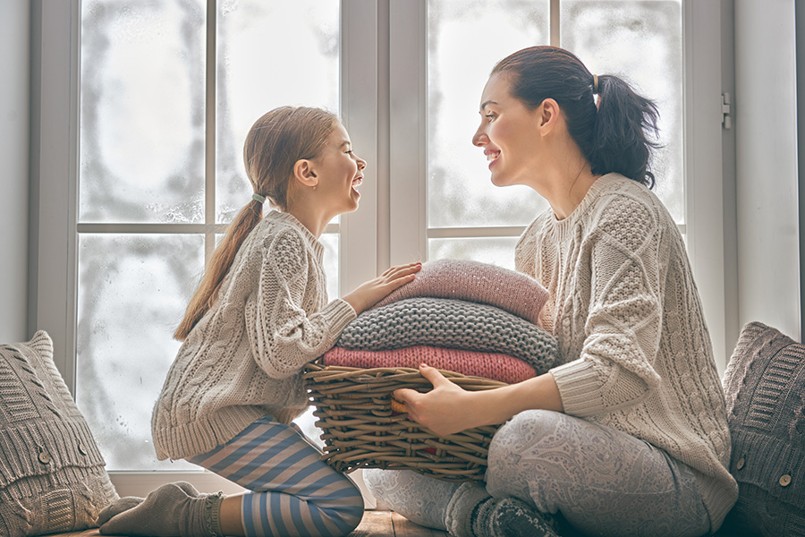 Mother and daughter sit in front of a snowy window smiling and laughing