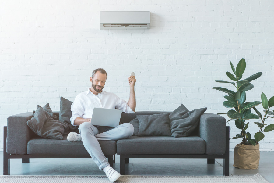 Man sitting on couch turning a wall air conditioner on with a remote